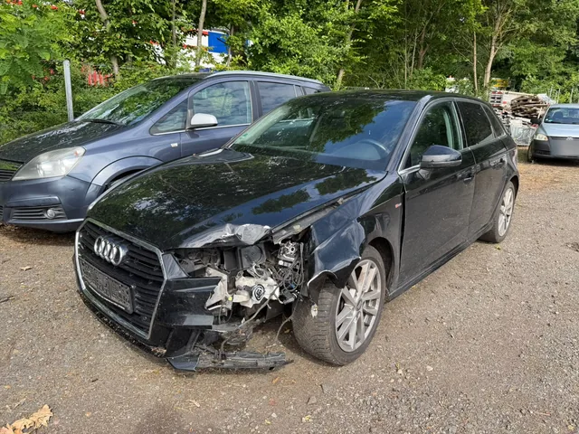 Dunkler Audi mit beschädigter Front und freiliegendem Scheinwerferbereich