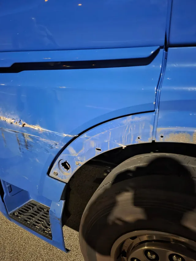 Schrammen und Verformungen am blauen Radlauf eines LKW